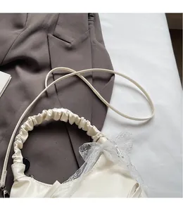 Detail of creamy white pleated handbag featuring a delicate lace bow and smooth shoulder strap