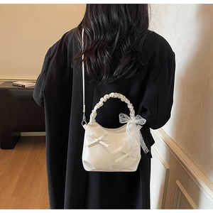 Detail of cream hobo bag with lace ribbon and ruffled handle on a black coat