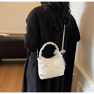 Detailed view of white pleated bow handbag with lace accents on black coat