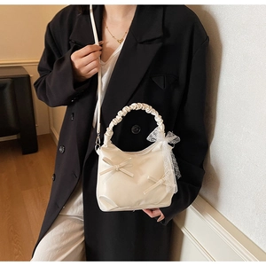 Detail of a beige bow-knot handbag with ruffled handle and lace butterfly charm
