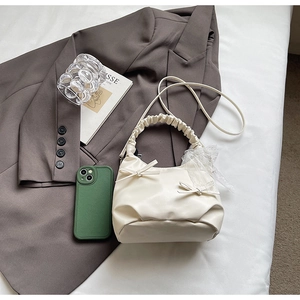 Détail du sac crème avec nœuds décoratifs, foulard en dentelle et poignées plissées
