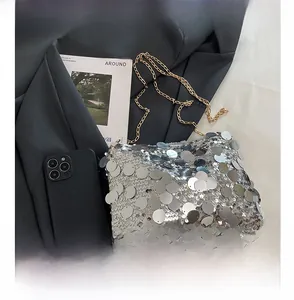 Detail of silver sequin crossbody bag with gold chain strap and textured surface