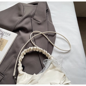 Détail du sac à main en cuir blanc crème avec nœuds en dentelle et poignée plissée