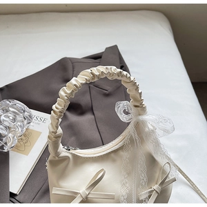 Détail du sac à main blanc crème avec nœuds en cuir, dentelle et anse plissée