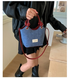 Dettaglio borsa a secchiello in denim blu con manico in pelle rossa e logo per donna