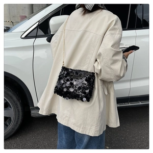 Street style shot of a black sequin crossbody bag with a gold chain strap on a model