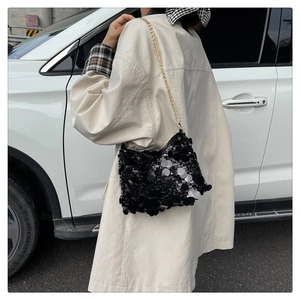 Detail of black sequin shoulder bag with gold chain strap worn by a model in daylight