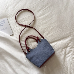 Dettaglio della borsa a secchiello in denim e pelle bordeaux con manico a nodo e rivetti