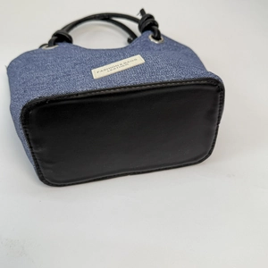 Dettaglio del tessuto denim blu e base in pelle nera della borsa a secchiello