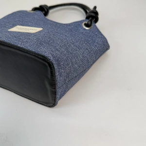 Dettaglio delle cuciture in denim blu e pelle nera sul fondo della borsa a secchiello