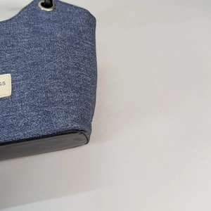 Dettaglio della borsa a tracolla in denim blu con etichetta GS e base in pelle nera