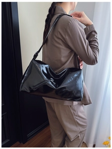 Side view of shiny black patent leather tote bag with silver zipper on female model