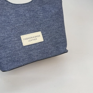 Dettaglio ravvicinato della trama denim blu e della toppa fashion su una borsa a secchiello