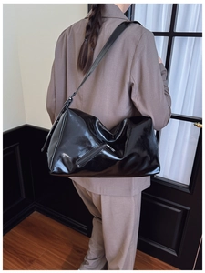 Close-up of a large black glossy pillow bag worn over the shoulder showing its supple drape