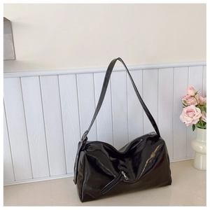 Detail of glossy black hobo bag with metal zipper and eyelet straps against a wall