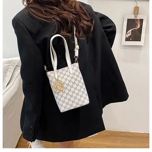 Detailed view of white bucket bag with M-pattern print and gold letter pendant