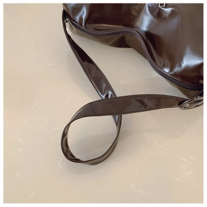 Detailed close-up of shiny chocolate brown patent leather handbag with silver hardware