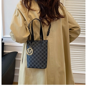 Detail of grey monogram tote bag with gold M pendant and black leather strap