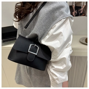 Détail du sac bandoulière noir minimaliste avec boucle argentée porté par un mannequin