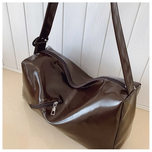 Detail of glossy brown patent leather shoulder bag with silver zipper and wide strap
