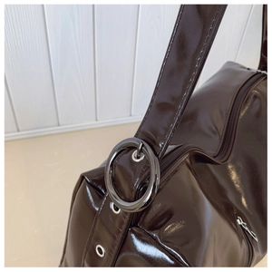 Detail showing the glossy dark brown patent leather and oversized black metal buckle