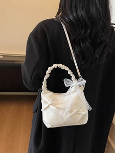 Sac à main blanc style balletcore avec nœuds en dentelle sur un manteau noir élégant
