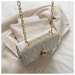 Detailansicht der weißen Stepptasche mit goldener Kette auf beigem ästhetischem Hintergrund
