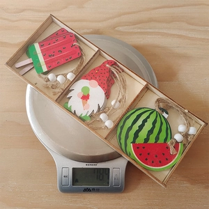 Three-grid wooden box with summer watermelon gnome ornaments on a kitchen scale