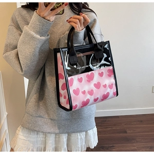 Detail of pink heart-print tote bag with transparent PVC panels and black handles