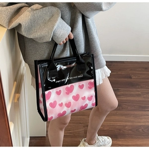 Detail of a pink heart print handbag with transparent top and black quote design
