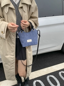 Borsa a secchiello in denim blu con manici tondi e tracolla abbinata a un trench beige