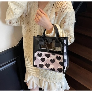 Detail of transparent tote bag featuring heart prints and black handles on a wooden staircase