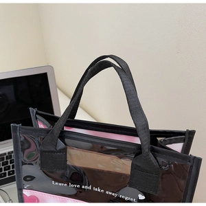 Detail of a semi-transparent PVC tote bag with pink heart prints and black handles