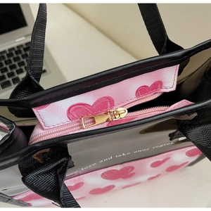 Close-up of black tote bag metal zipper and pink heart print with slogan detail