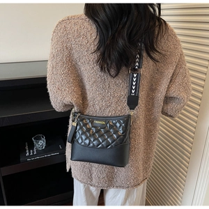 Detail of black quilted crossbody bag featuring a patterned wide strap and fashion patch