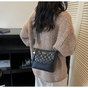 Detail of quilted leather crossbody bag featuring wide geometric strap and fringe charm
