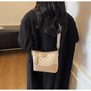 Detail of beige quilted leather handbag with wide fabric strap and fashion metal logo