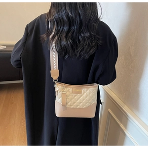 Detail of beige quilted crossbody bag with FASHION metal plate on a black coat