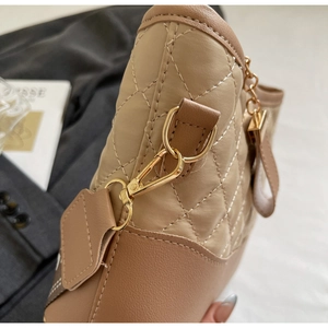 Detail shot of golden metal clasp and quilted stitching on beige leather handbag