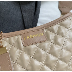 Detailed close-up of quilted beige handbag featuring gold FASHION embroidery and chain