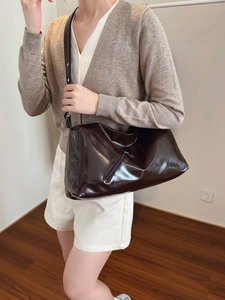 Large dark brown glossy pillow handbag with adjustable wide strap shown on a model