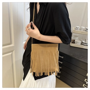 Detail of camel suede crossbody bag with long tassels on a stylish female model
