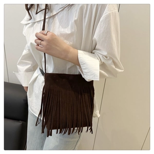 Detail of dark brown suede shoulder bag featuring bohemian fringe and minimalist strap