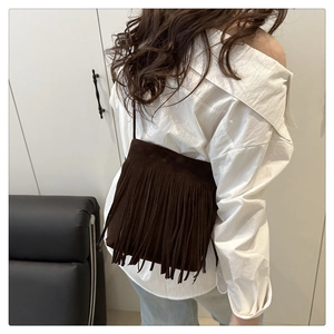 Detailed view of dark brown suede fringe shoulder bag worn by a model in a casual setting