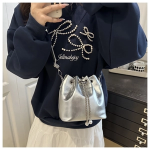 Detail of silver metallic bucket bag with chain drawstring and pearl accents on shoulder
