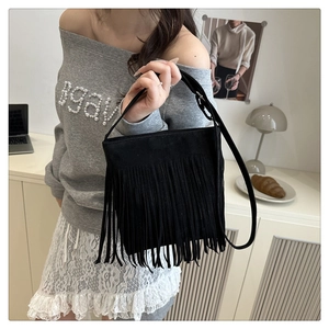 Detail of black suede handbag with long fringe tassels shown on a shoulder strap
