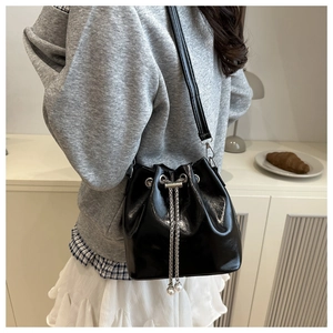 Detail of a black drawstring bucket bag with silver chain and pearl accents on a model