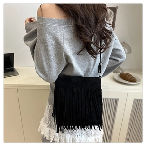 Detailed view of the soft black suede texture and long hanging tassels on the crossbody bag