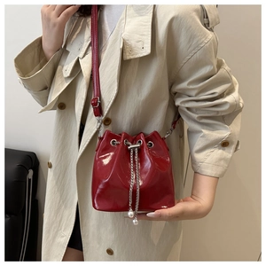 Detail of red glossy bucket bag with drawstring pearls and silver chain closure