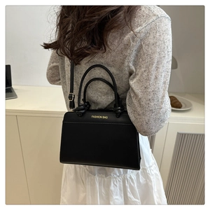 Detailed view of black leather handbag worn cross-body with elegant casual outfit